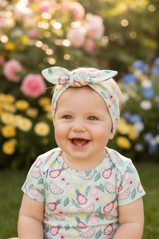 Close-up van babymeisje met haarband tropics aop en romper tropics aop in een zomerse setting