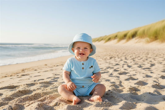 Baby in azure terry outfit op een echt strand met duinen en zee op de achtergrond