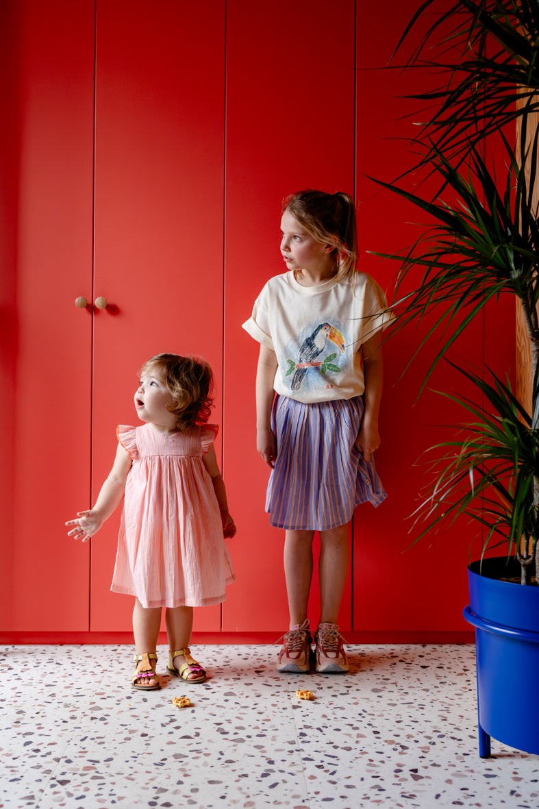 Meisje draagt lichtroze jurk met fluo strepen met groter meisje in blauw