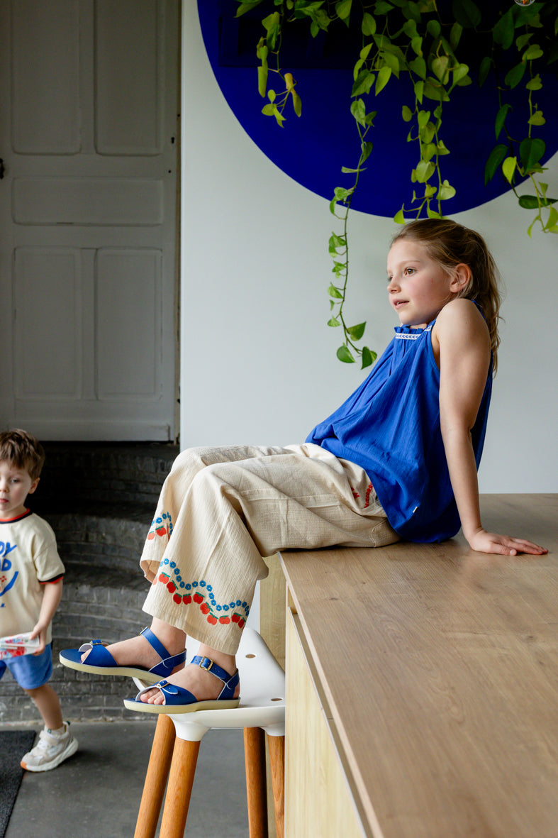 Meisje draagt cobaltblauw topje met ecru broek met geborduurde figuren

