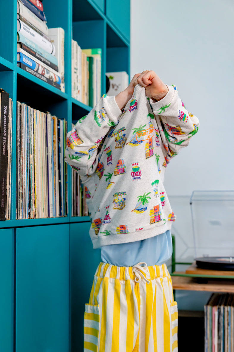 Kind draagt ecru sweater met zomerse print en geel gestreepte denim broek