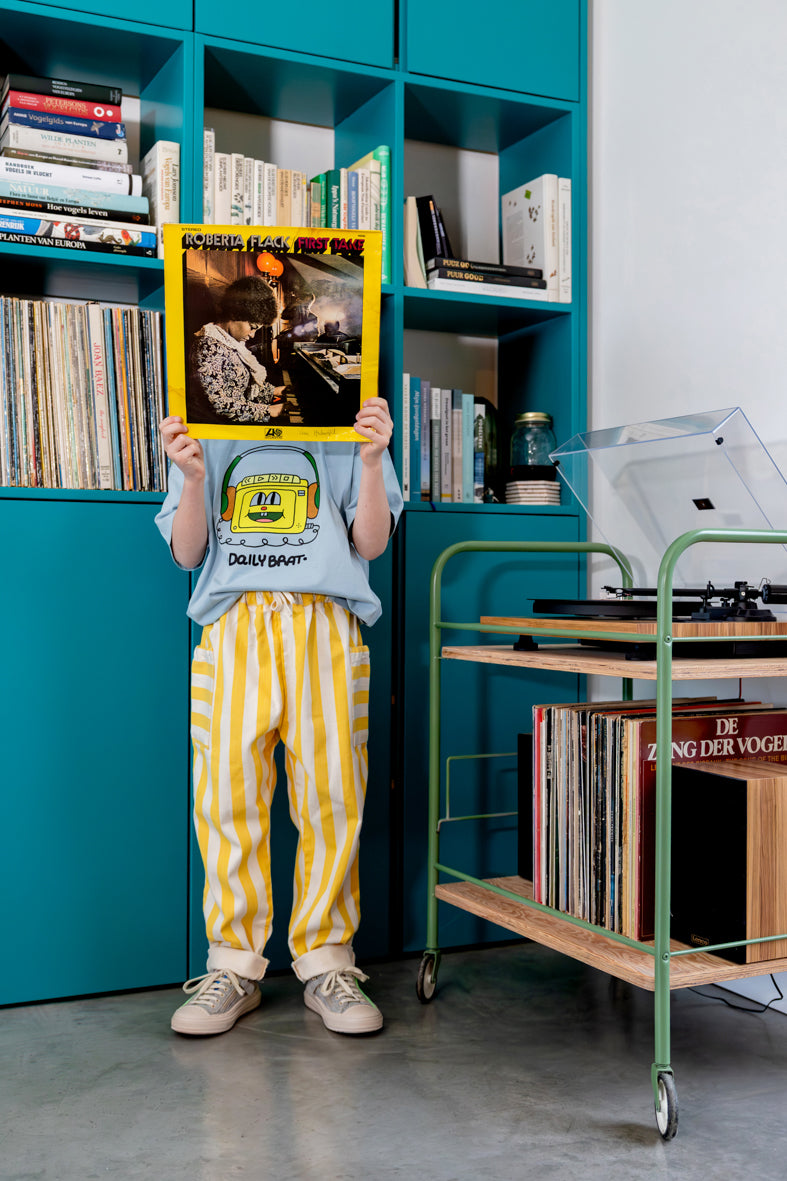 Jongen draagt lichtblauw t-shirt met hoofdtelefoon print en geel gestreepte denim broek
