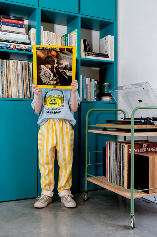 Jongen draagt lichtblauw t-shirt met hoofdtelefoon print en geel gestreepte denim broek
