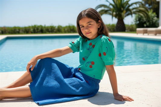 Meisje draagt groen t-shirt met kersen
 koningsblauwe tetra rok
