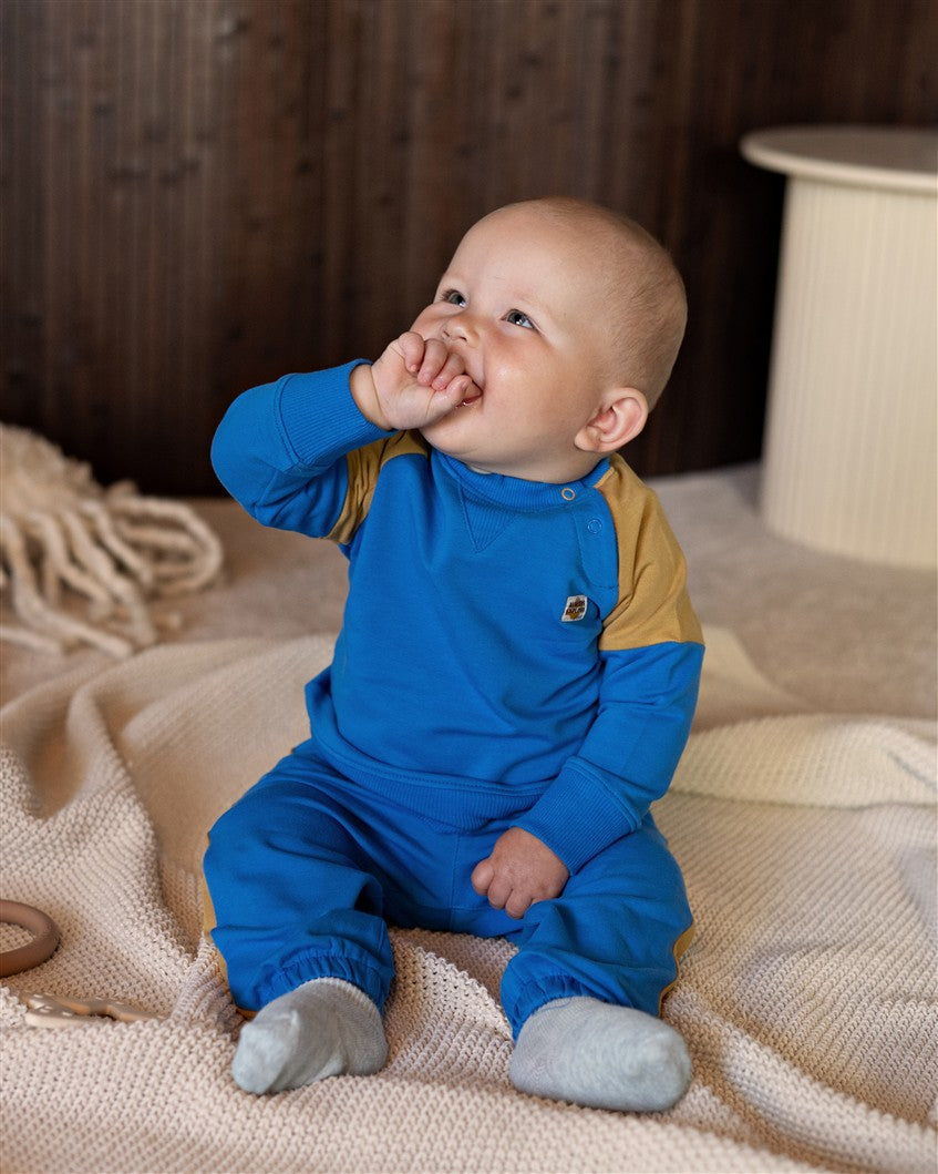 Blauwe babysweater met gele details op de schouders.